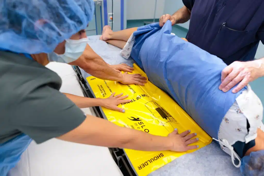 Medical professionals in an operating room moving a patient with a disposable slide sheet